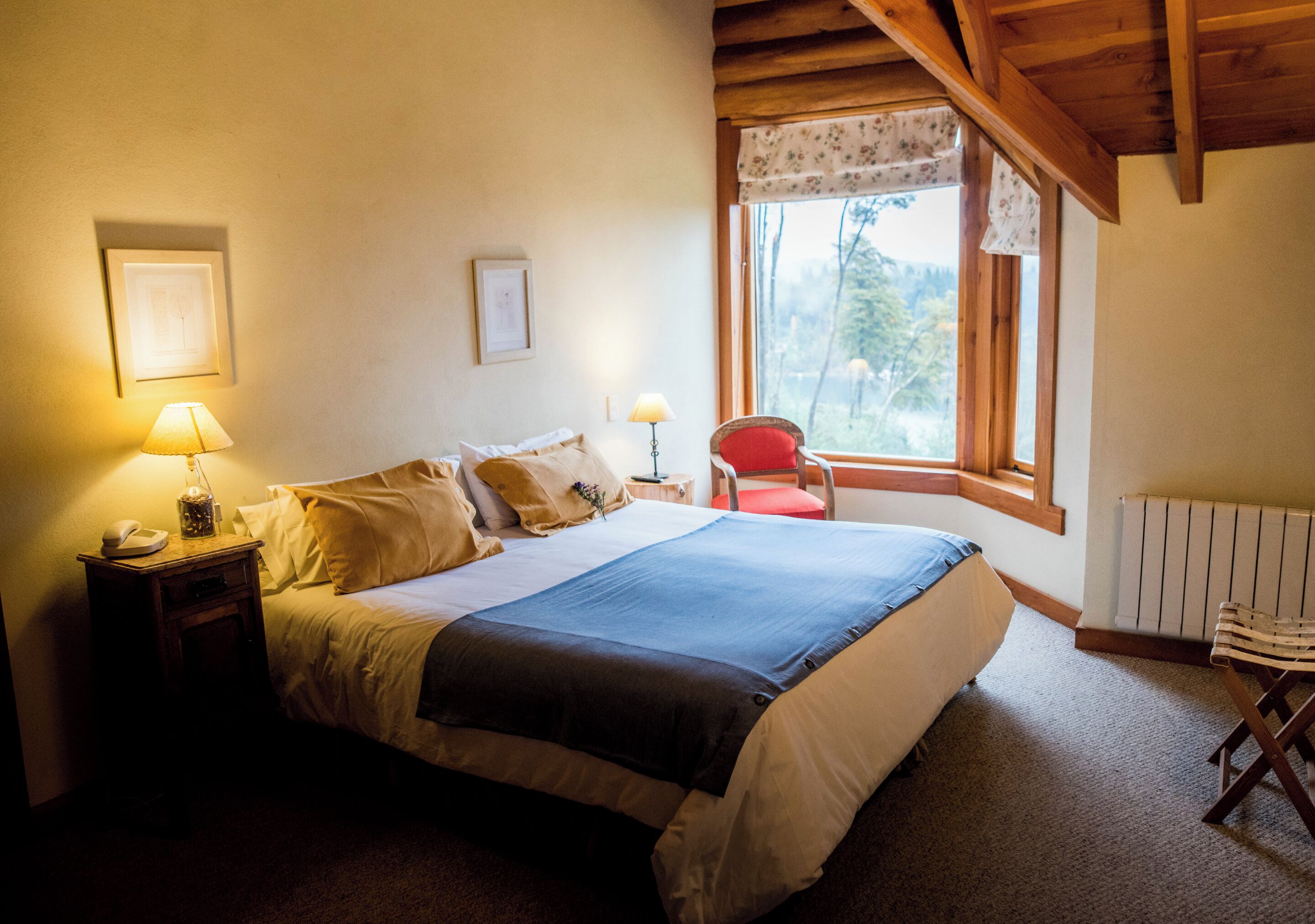 Ein Schlafzimmer mit einem großen Bett, Nachttischlampen, einem Sessel, einem Fenster mit Blick und einer Heizung.