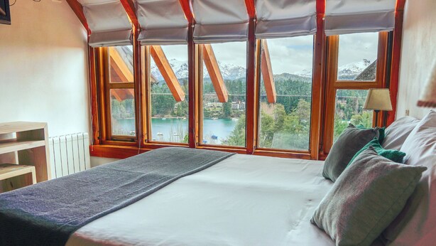 A bedroom with a large bed, a view of a lake and mountains, and wooden beams. - El Bosque by DOT Tradition (Villa La Angostura)