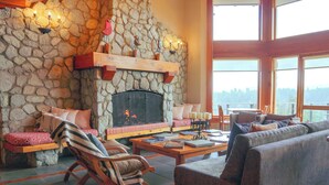 A cozy living room with a stone fireplace, comfortable seating, and large windows offering a view. - El Bosque by DOT Tradition (Villa La Angostura)