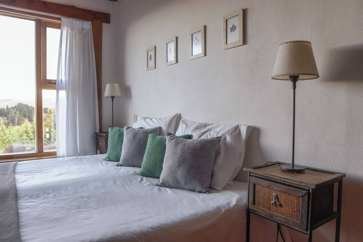 Un lit bien fait, avec des oreillers blancs et verts, une lampe de chevet et un tableau encadré au mur.