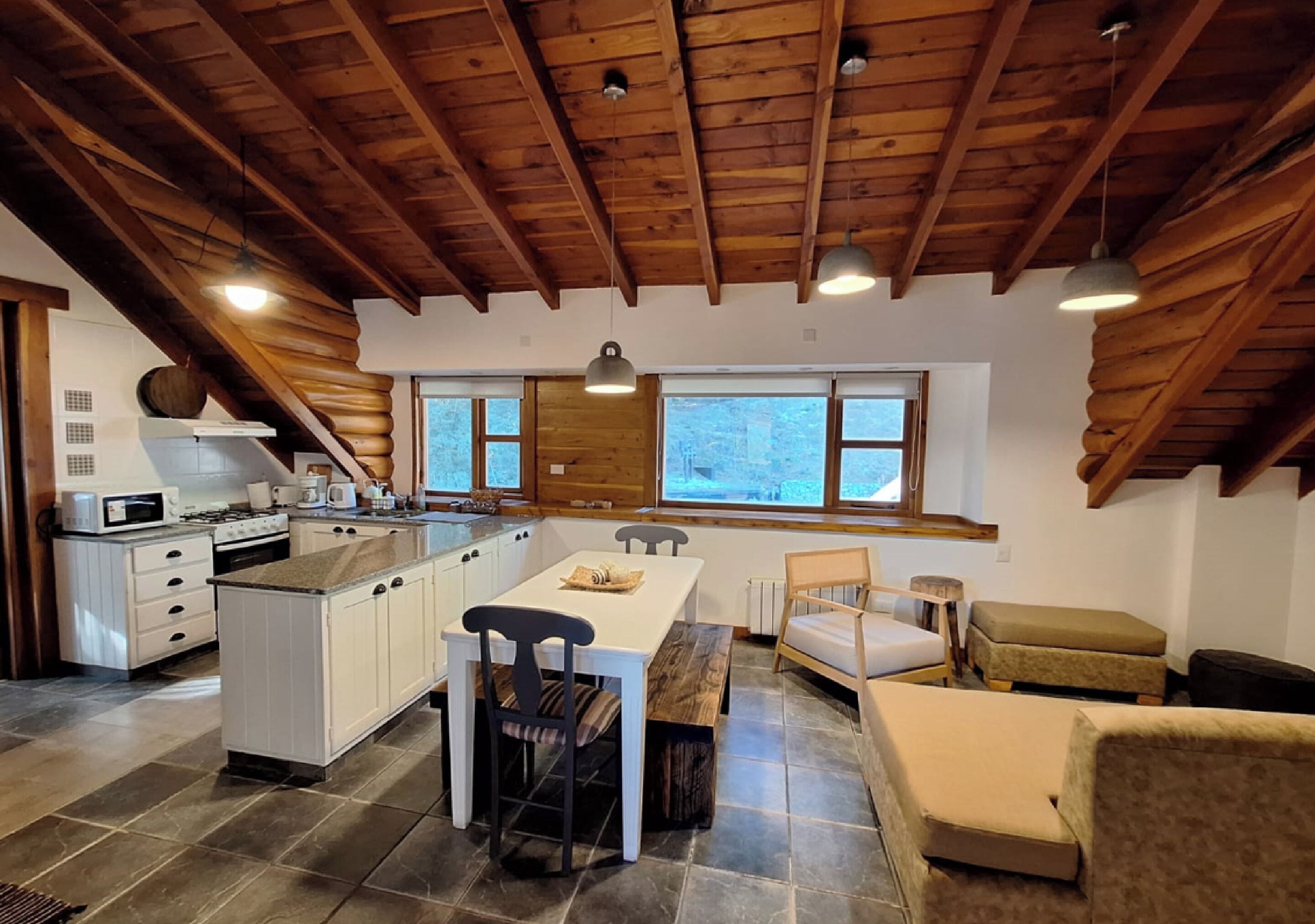 Una cocina amplia con una isla grande, vigas de techo de madera y vistas al exterior a través de ventanas grandes.
