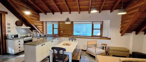 Una cocina amplia con una isla grande, vigas de techo de madera y vistas al exterior a través de ventanas grandes.