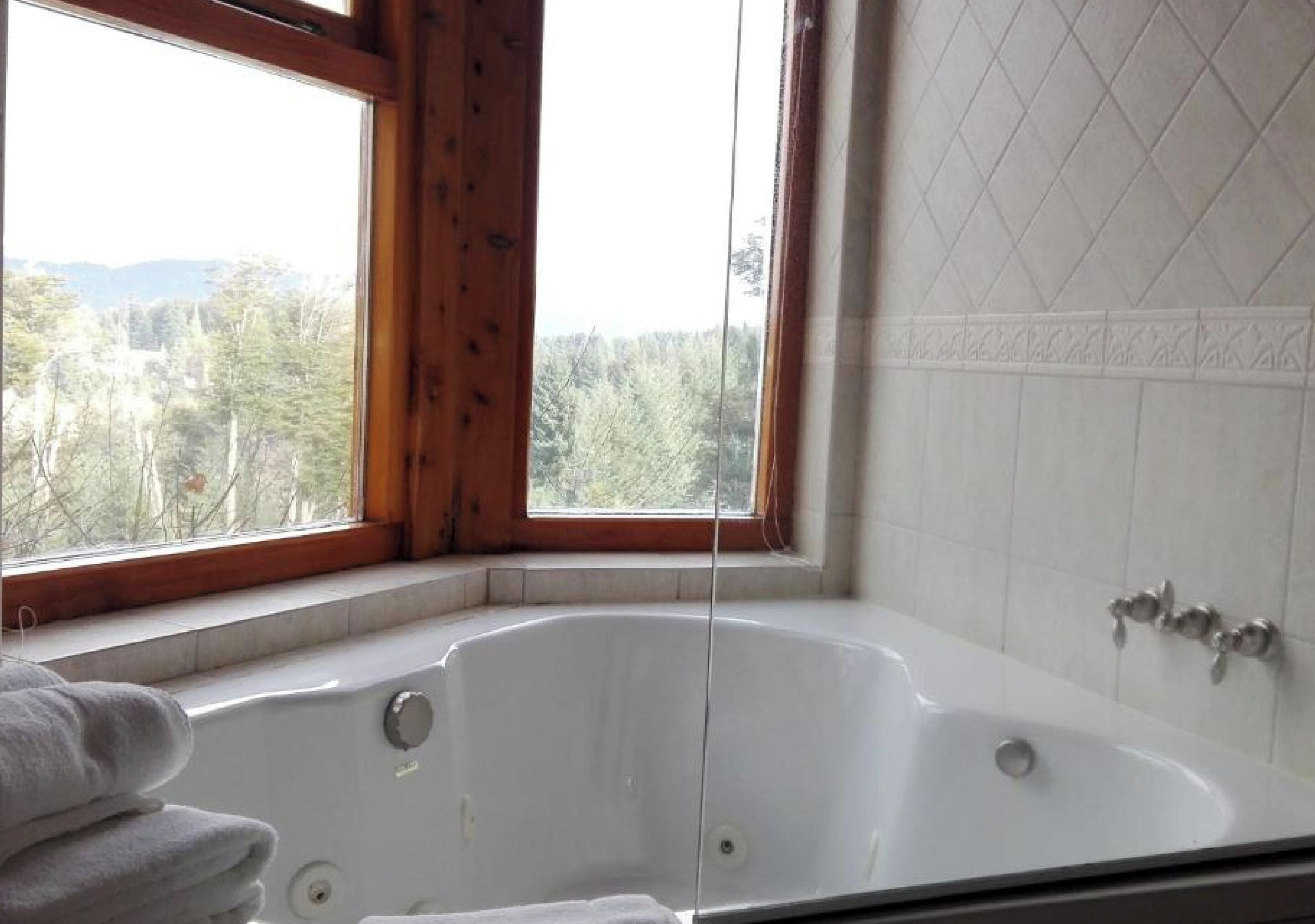 Un baño con una bañera grande, una ventana con vistas a árboles y una pared de azulejos.