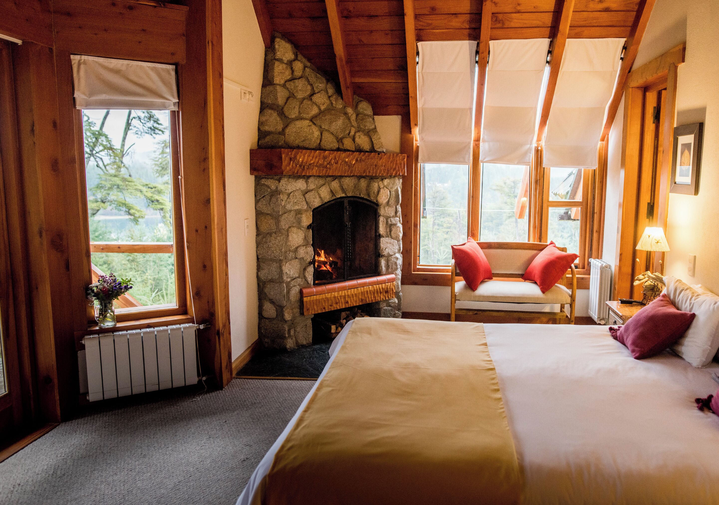 Una habitación acogedora con chimenea de piedra, una cama, un sillón y vistas al exterior.