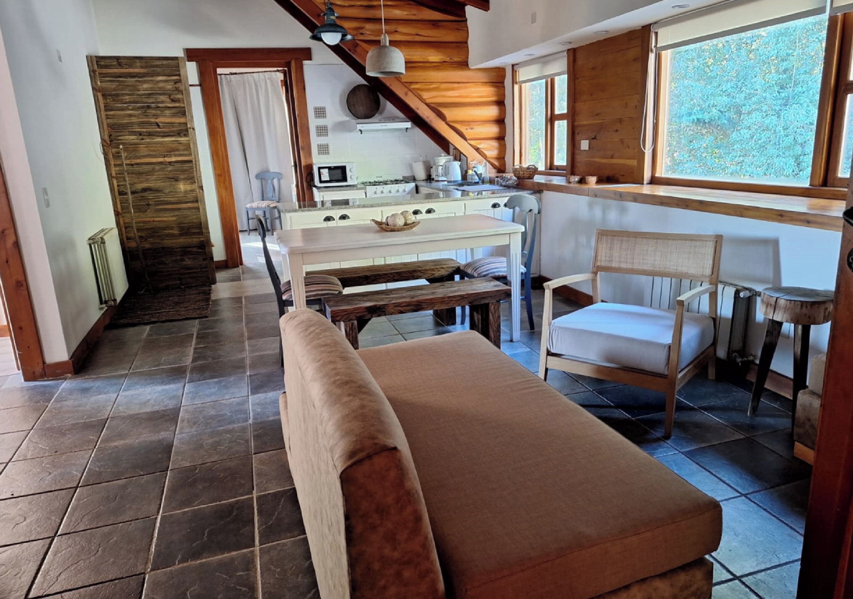 A cozy kitchen with a dining area, a bench, and a window with a view of trees.