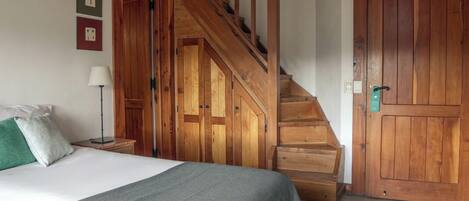 Un dormitorio con una escalera de madera, una cama con un edredón gris, una mesita de noche con una lámpara y dos cuadros en la pared.