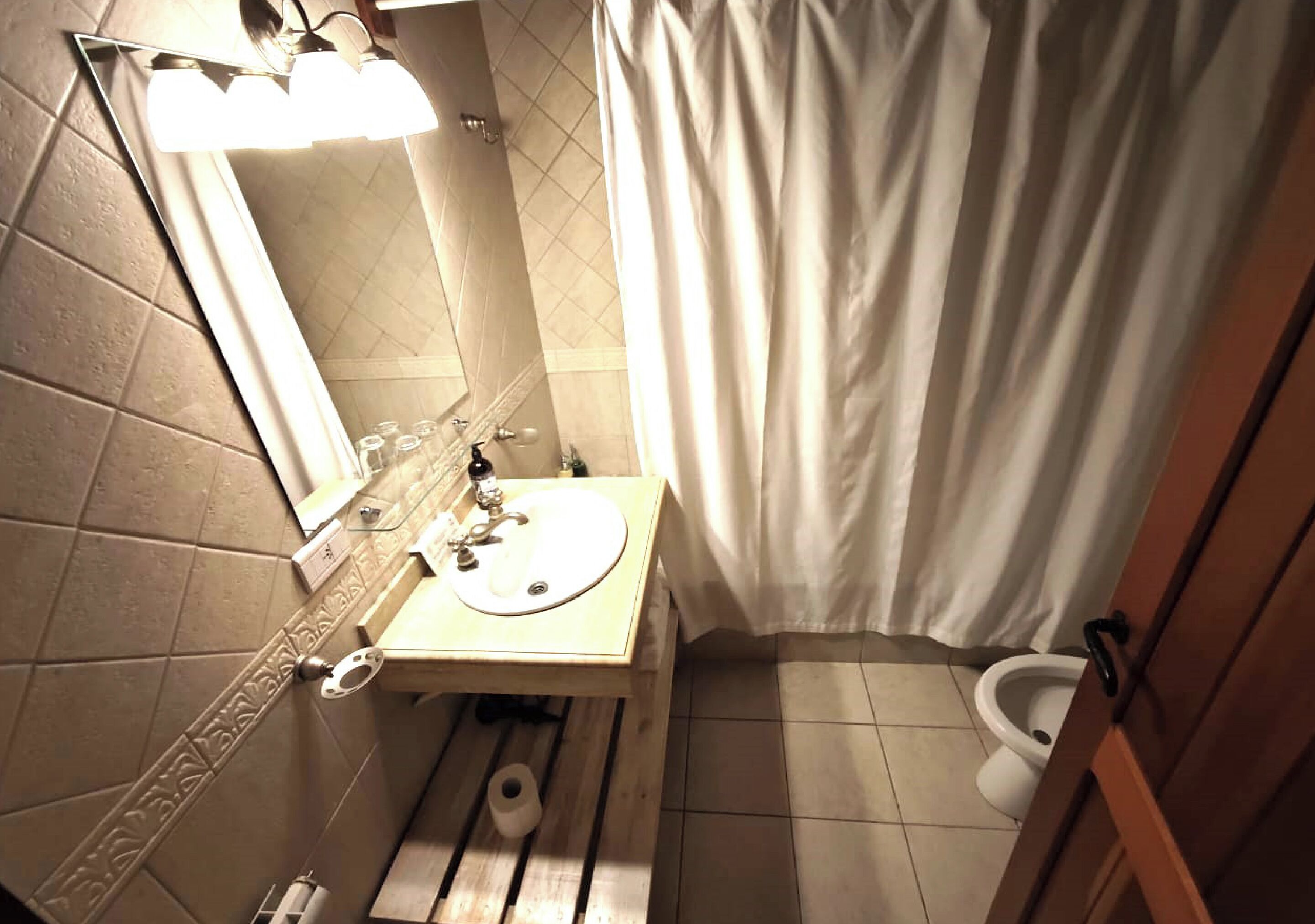 A bathroom with a wooden vanity, a mirror, a sink, a toilet, and a shower curtain.