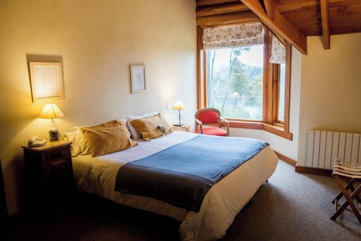A bedroom with a bed, bedside lamps, a chair, a window, and a radiator.