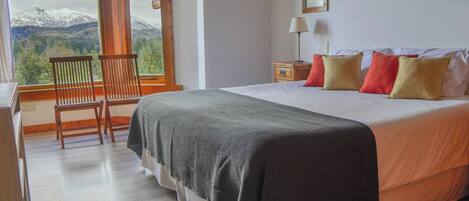 A bedroom with a bed, a chair, a nightstand, a lamp, and a window with a mountain view.