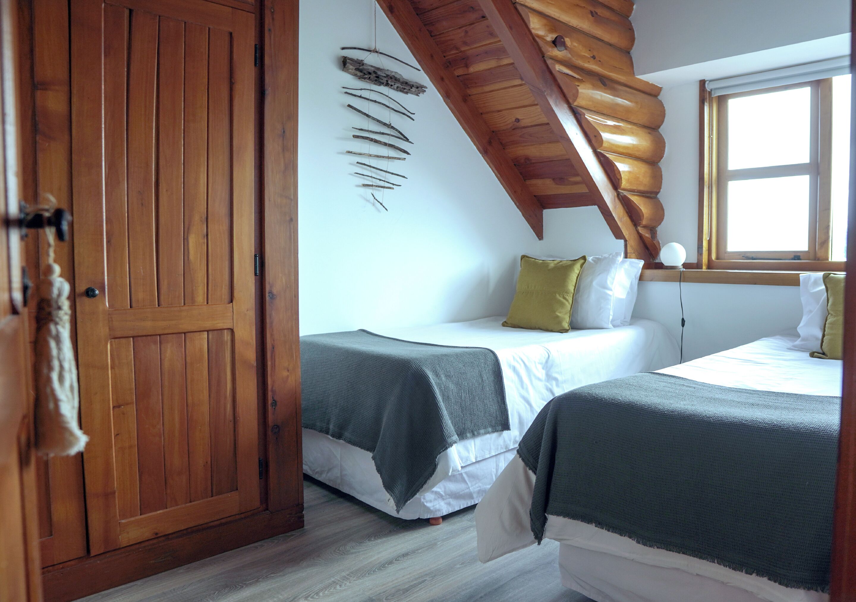 A room with two beds, wooden beams, a window, and a wall-mounted decoration.