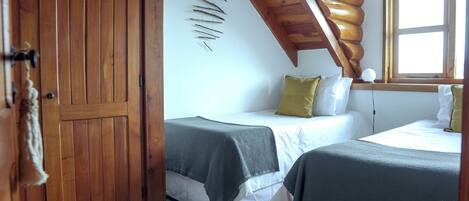 A room with two beds, wooden beams, a window, and a wall-mounted decoration.