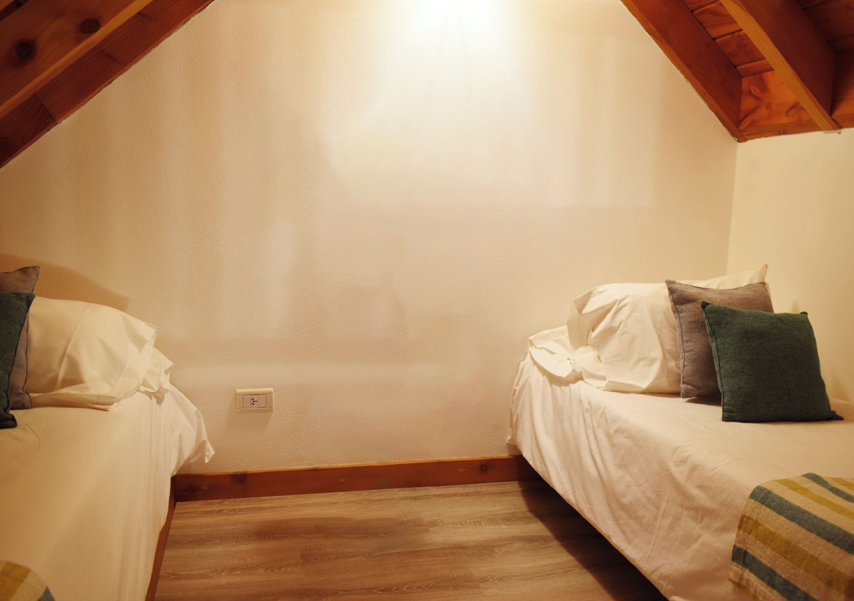 Une petite pièce agréable, dotée de deux lits, d’un plancher en bois et d’un plafond en pente.