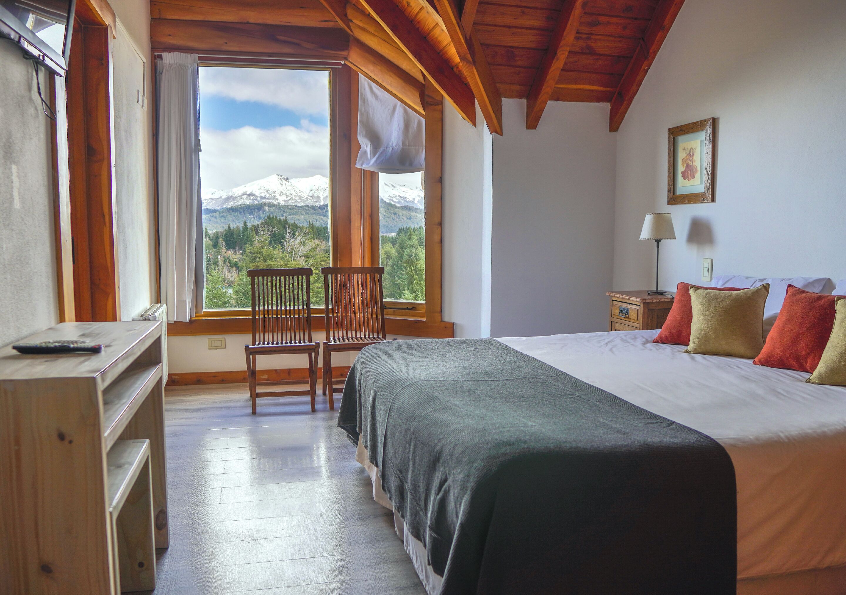 A bedroom with a bed, a desk, a chair, a nightstand, and a window with a mountain view.