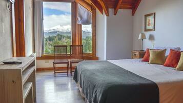 A bedroom with a bed, a desk, a chair, a nightstand, and a window with a mountain view.