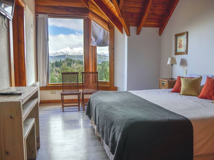 A bedroom with a bed, a desk, a chair, a nightstand, and a window with a mountain view.