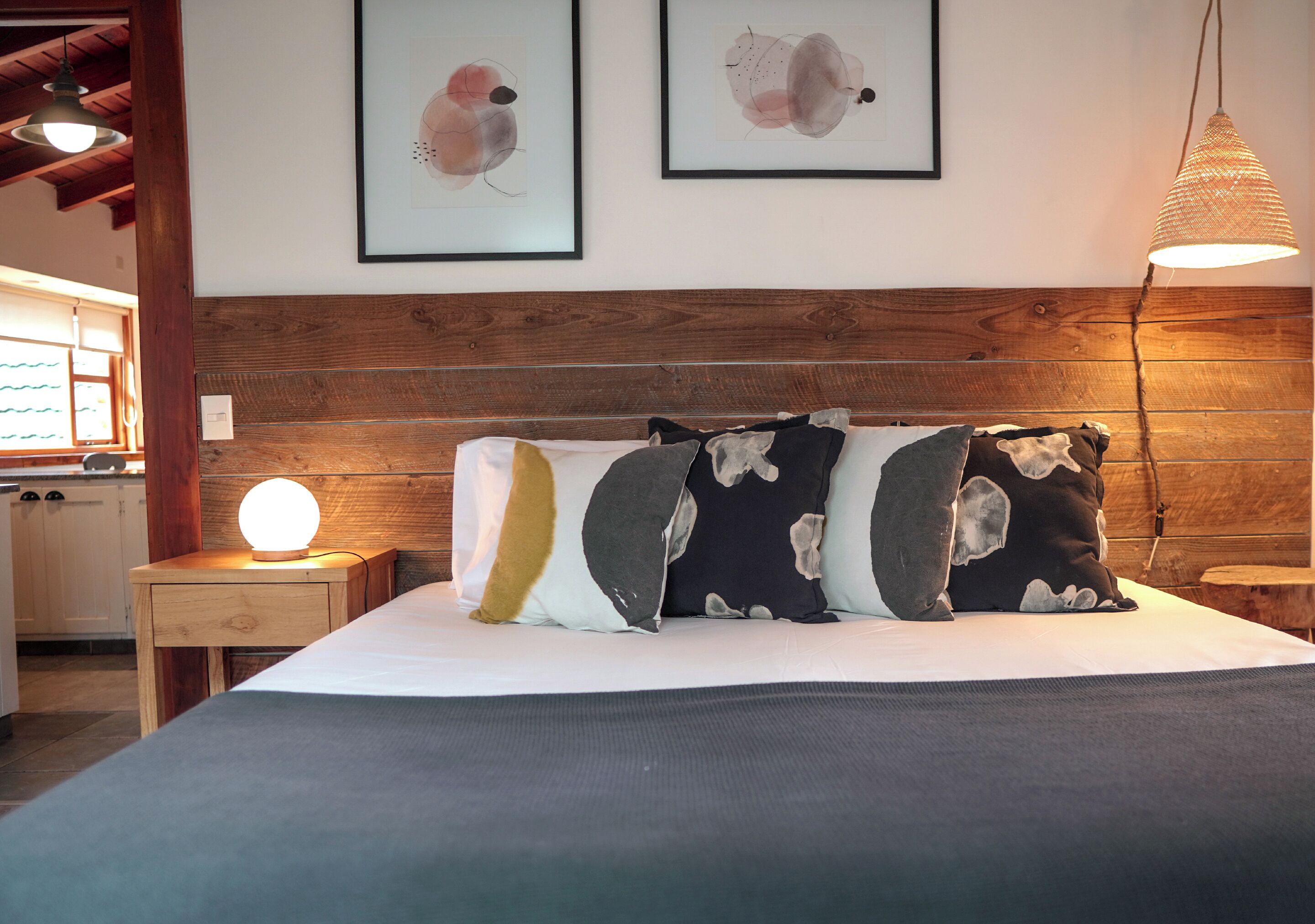 A neatly made bed with a wooden headboard, a bedside lamp, and two framed abstract artworks on the wall.