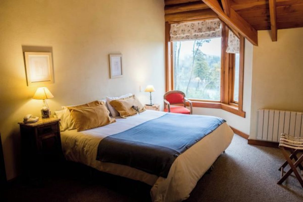 A bedroom with a bed, bedside lamps, a chair, a window, and a radiator.