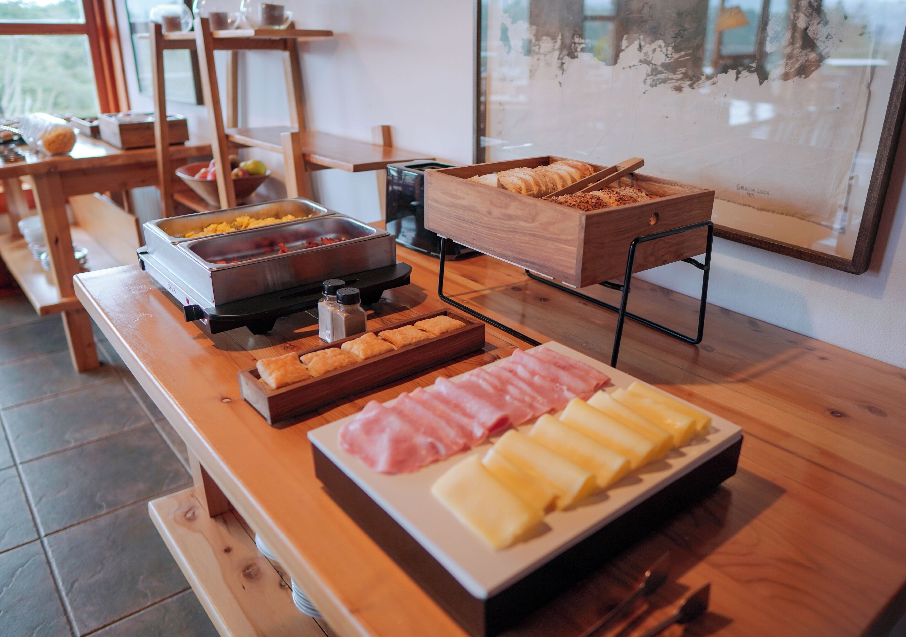 Montaje de buffet con diversos alimentos, incluyendo carnes, quesos y pastelería.