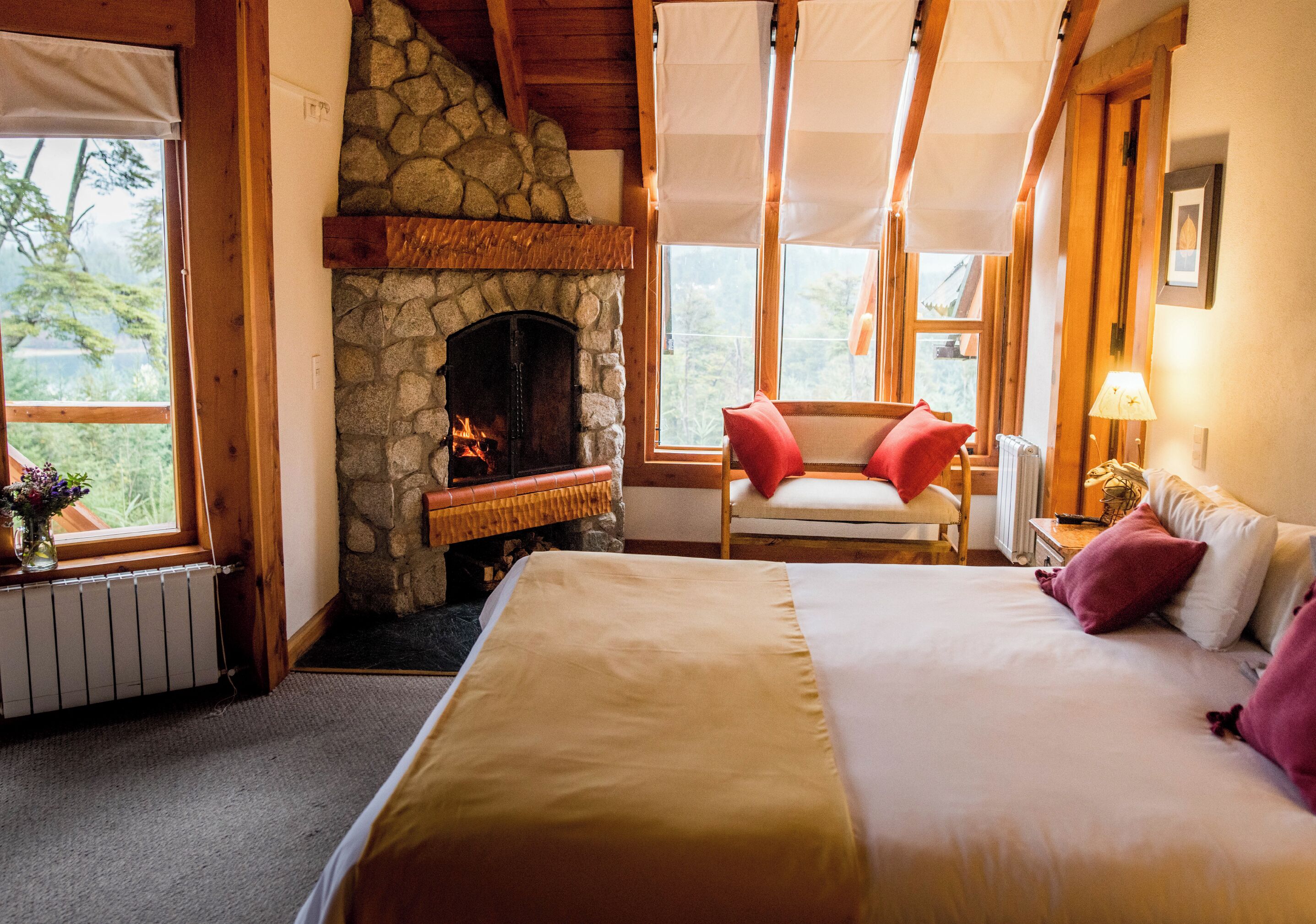 A cozy bedroom with a stone fireplace, a large bed, a chair, and a window with curtains.