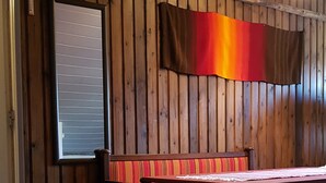 A room with wooden panel walls, a bench with a striped cushion, a table with a white placemat, and a red flag. - Hostel Sivakka (Kolari)