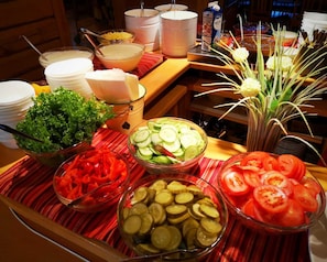 A buffet table with various food items including salads, sliced cucumbers, tomatoes, and pickles.