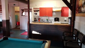 A pool area with a wooden pool table, a kitchen with red cabinets, and a dining area with striped chairs. - Hostel Sivakka (Kolari)
