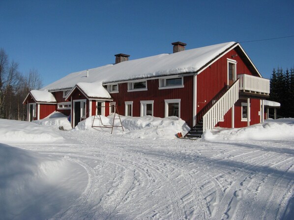 A red wooden house with a snow-covered roof and a staircase leading to the entrance.