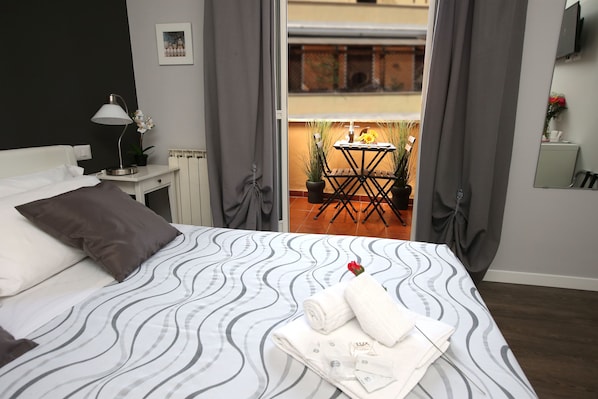 Ein ordentlich bezogenes Bett mit einem gemusterten Überwurf, einer Nachttischlampe und einem kleinen Tisch mit Topfpflanze und Blumenvase.