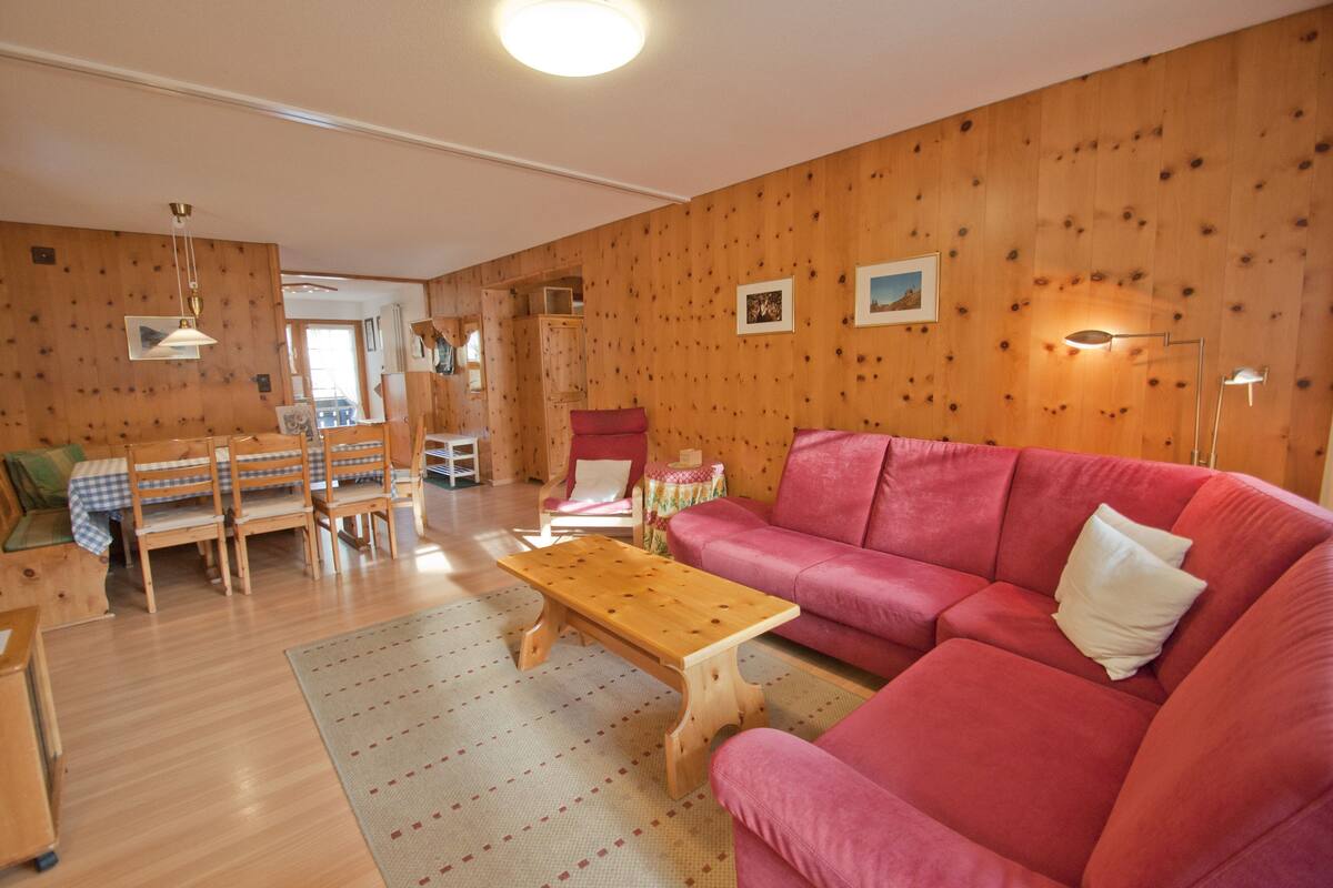 Un salón acogedor con paredes de madera, un sofá rojo, una mesa de centro de madera y un comedor con mesa y sillas.