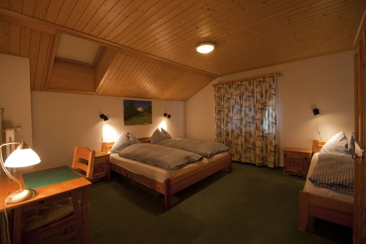 Un dormitorio acogedor con techo de madera, un escritorio con lámpara, dos camas con ropa de cama a cuadros y un cuadro en la pared.