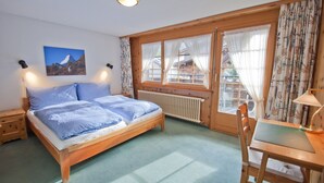 Un dormitorio con una cama de madera, un escritorio y una silla. Hay una ventana con cortinas y un cuadro en la pared.