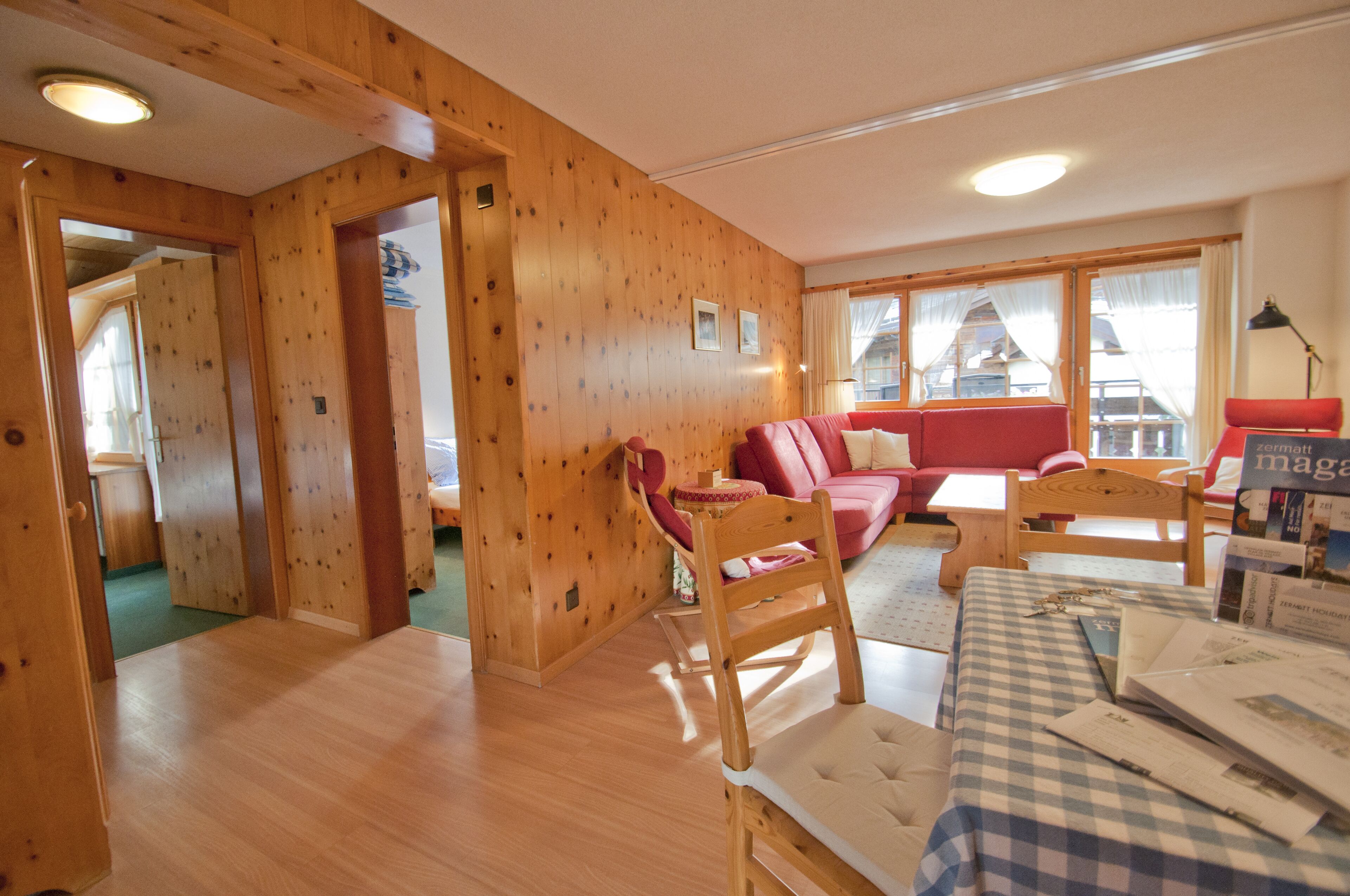 A wooden-paneled room with a red sofa, a wooden table, and a checkered tablecloth.