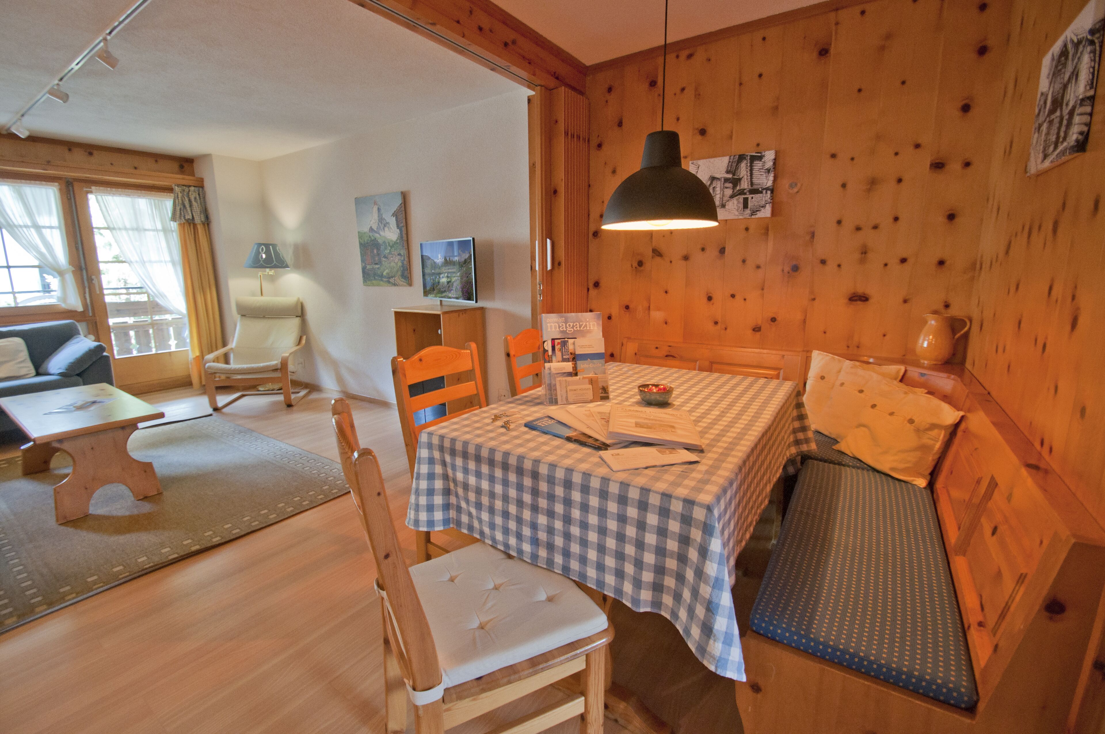 A cozy room with a checkered table, wooden walls, a sofa, and a dining area.