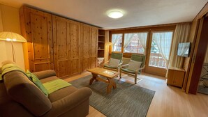 Una sala de estar acogedora con un sofá marrón, dos sillones verdes, un mueble de madera y una mesita.