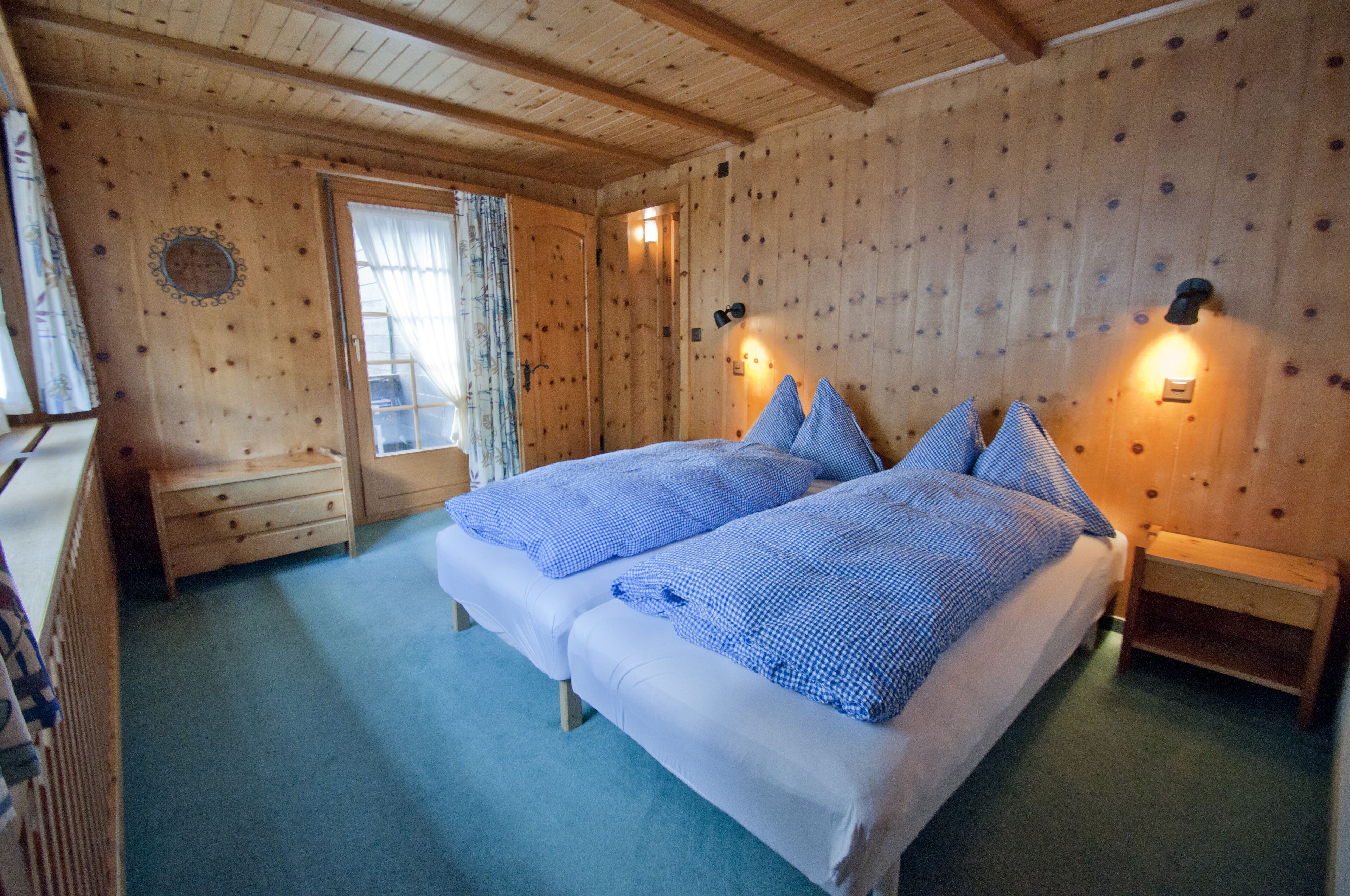 A wooden room with two beds, a small table, and a window with curtains.