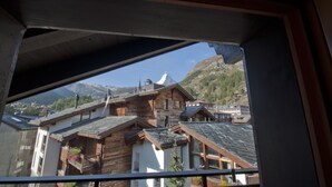 Vista desde una ventana que da a edificios tradicionales de madera con techos inclinados, con montañas al fondo.