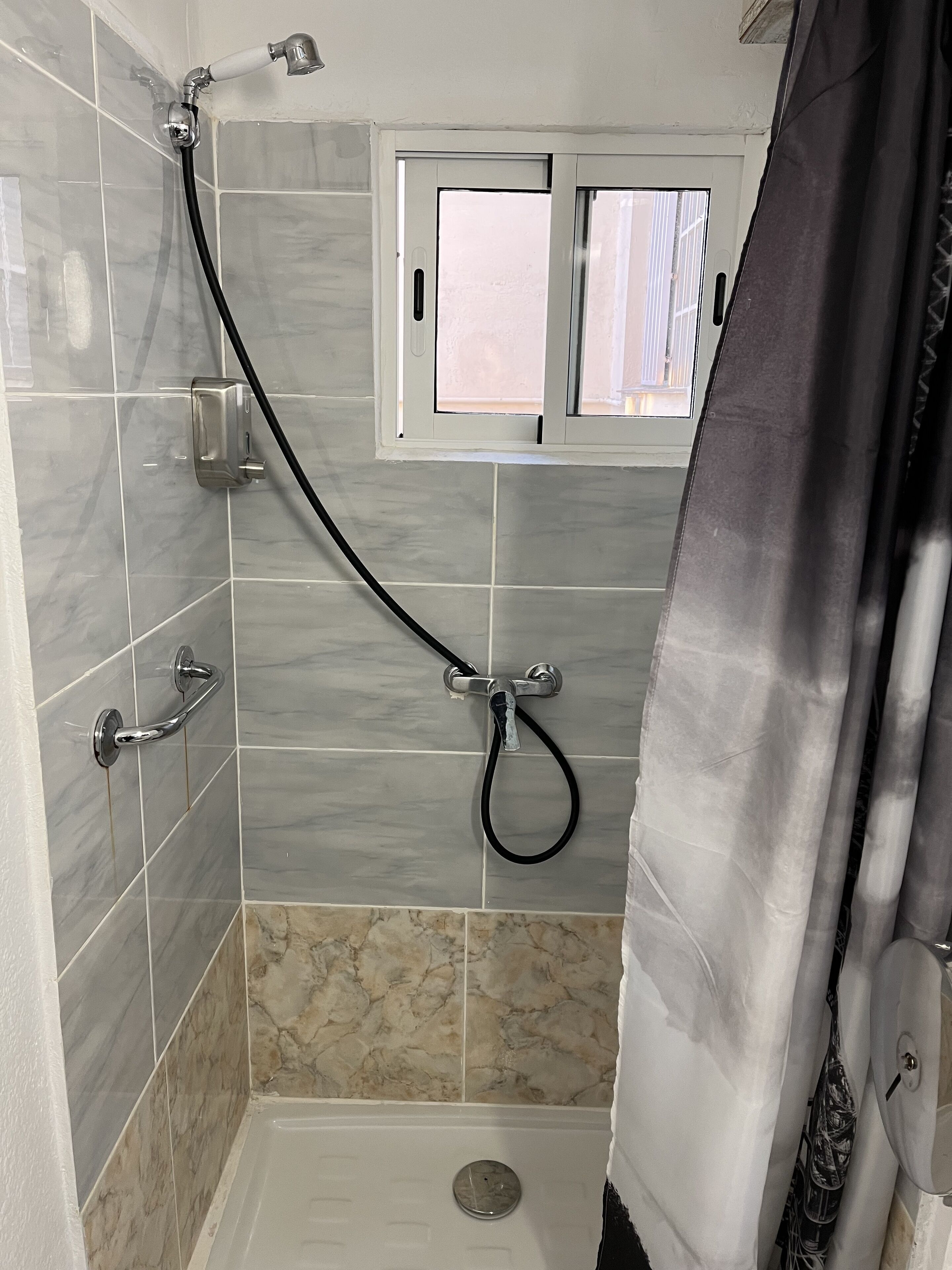 Eine Dusche mit Handbrause, einem Fenster und einem gefliesten Boden.