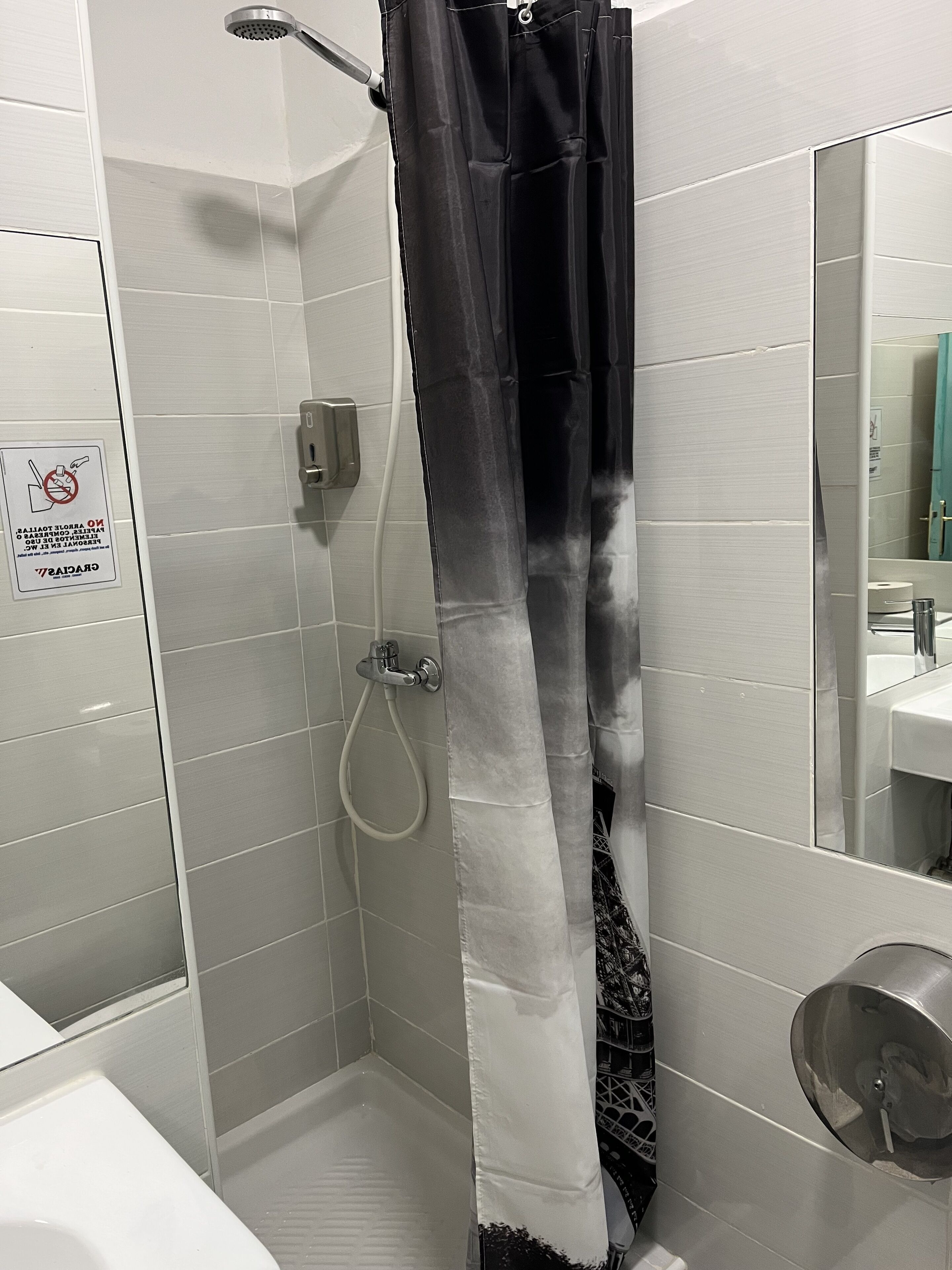 Un área de ducha con cortina de ducha blanco y negro, un cabezal de ducha manual y un grifo empotrado en la pared.