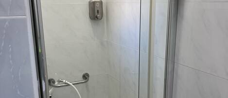 Een douchecabine met glazen wanden, een handdouche, een zeepdispenser en een handgreep.