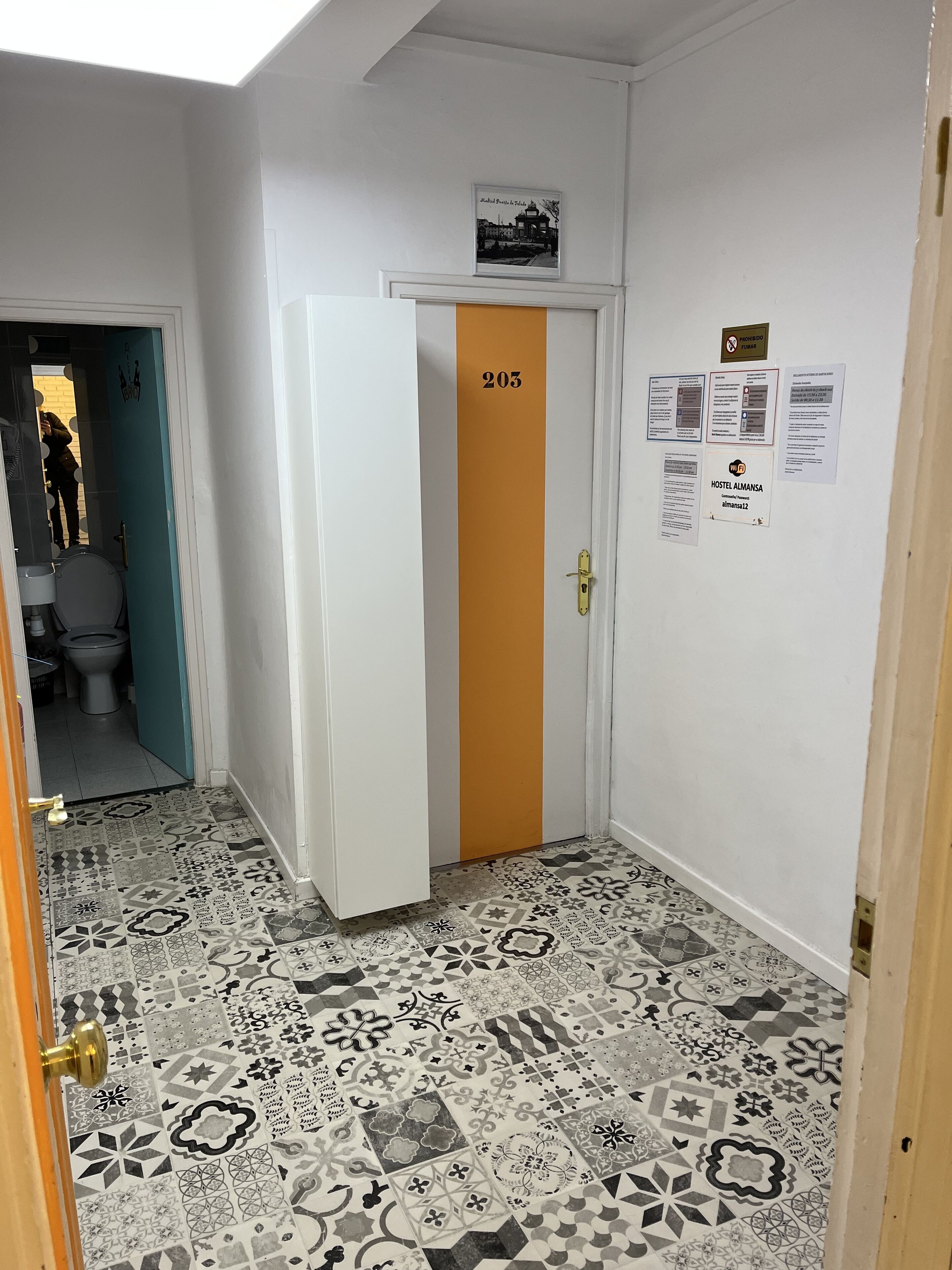 A hallway with a door labeled 203, a patterned floor, and several informational posters on the wall.
