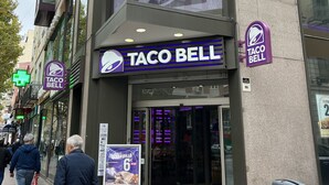 A Taco Bell restaurant with a large sign, a glass entrance, and a trash can on the sidewalk. - Casa de huespedes Almansa (Madrid)