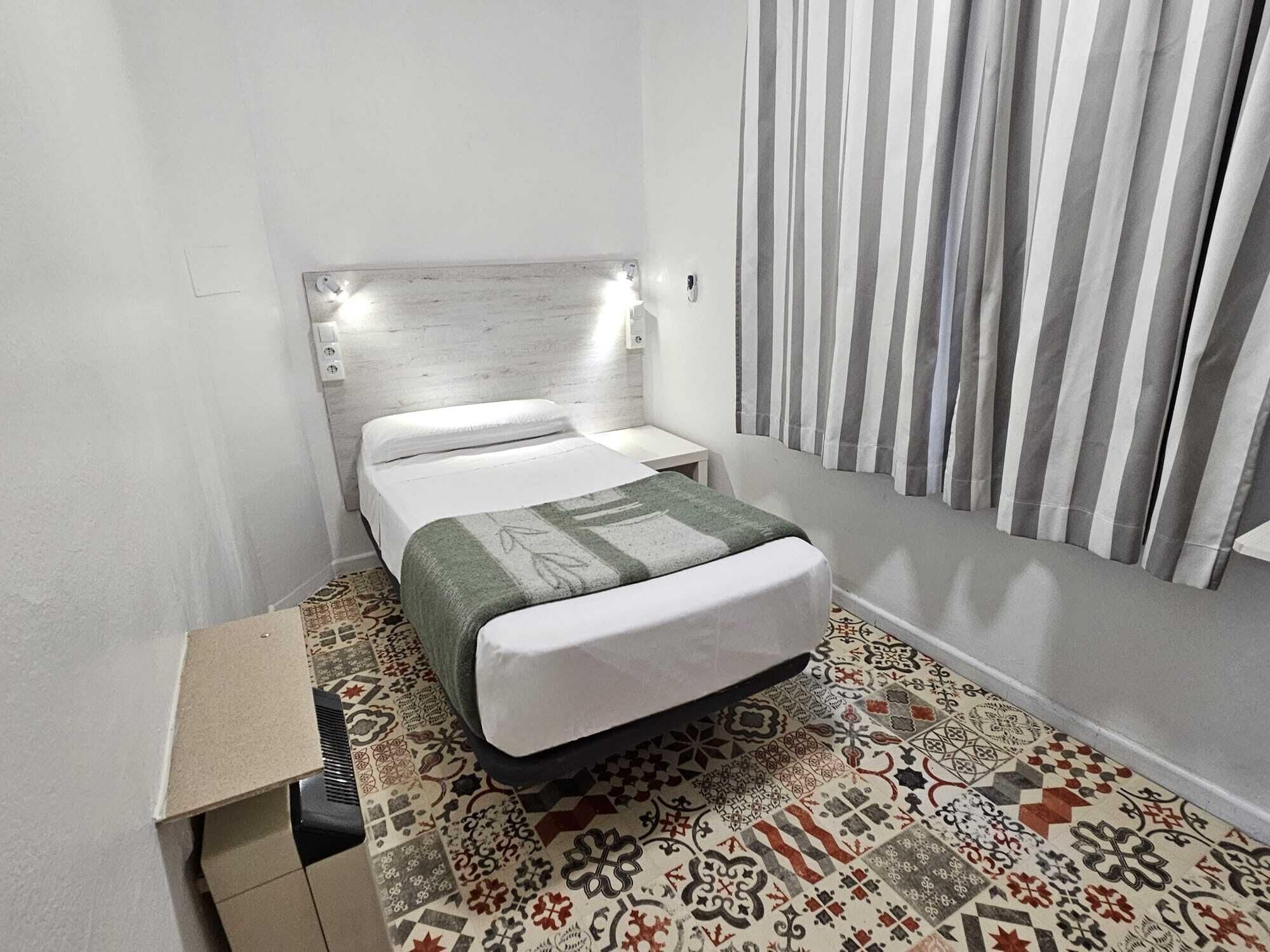 A small, neatly arranged bedroom with a bed, a bedside table, and a headboard with lights.