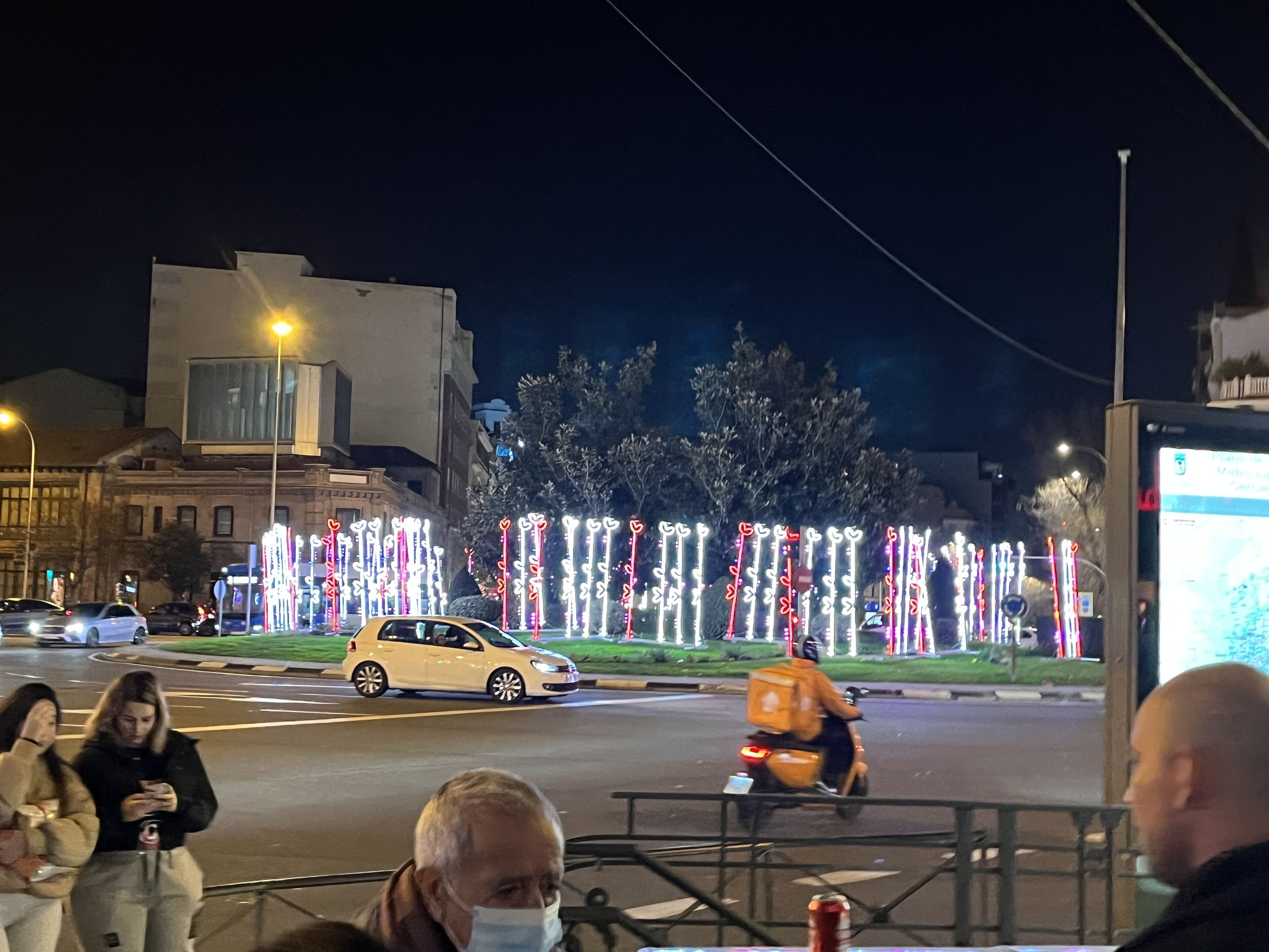 A street scene at night with illuminated decorations and a few vehicles.