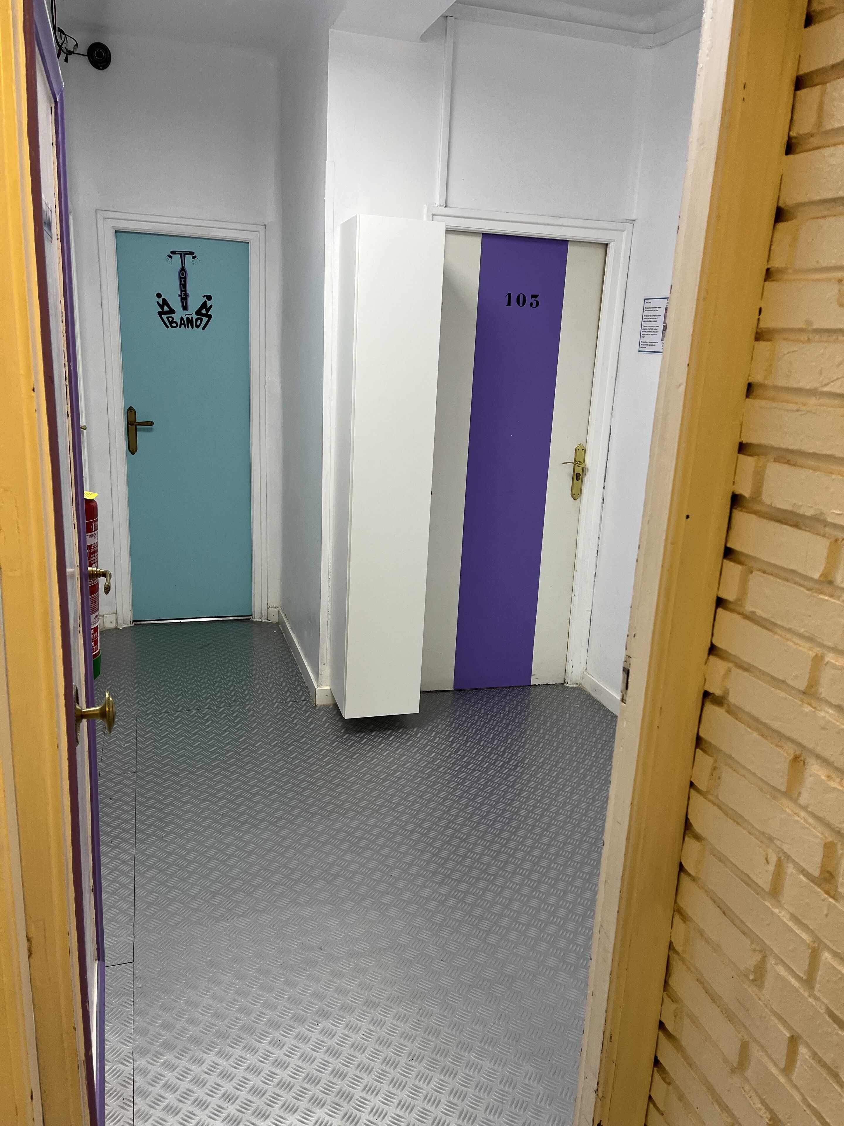 Un pasillo con dos puertas, una azul turquesa y otra morada, ambas con números.