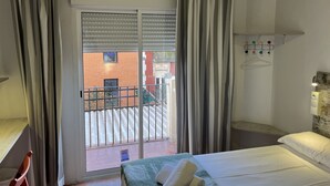 A hotel room with a bed, a window with curtains, a view of the outside, and a small table with a chair. - Casa de huespedes Almansa (Madrid)