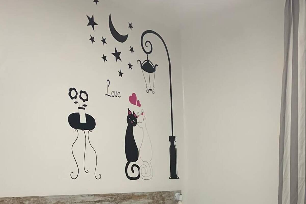 A bedroom with a bed, a nightstand, a chair, and a wall decoration featuring a cat and a moon.