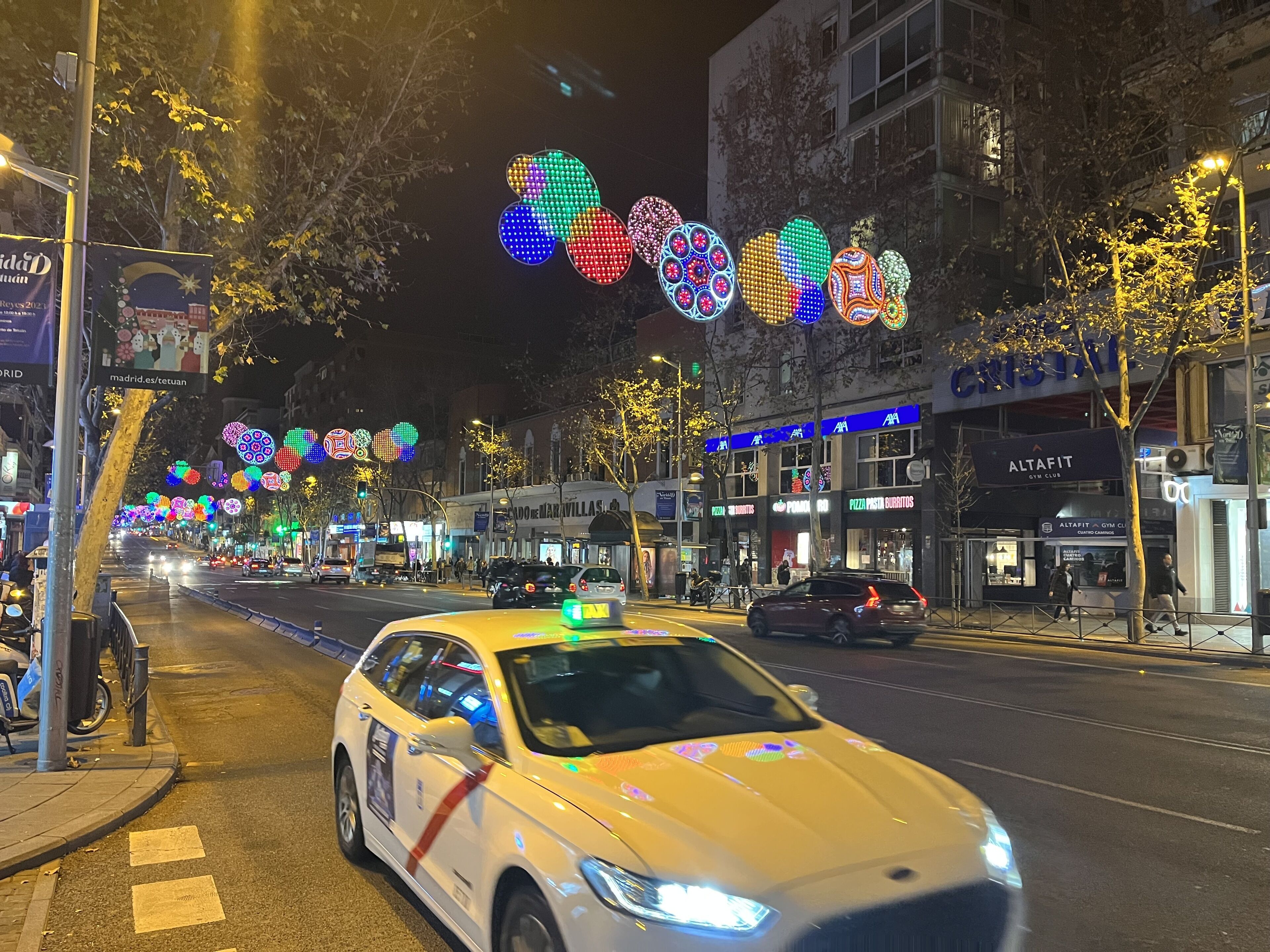 A street with illuminated decorations and a white taxi.