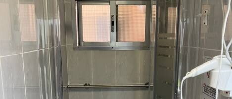 A glass-enclosed shower stall with a control panel, a towel rack, and a hand dryer.