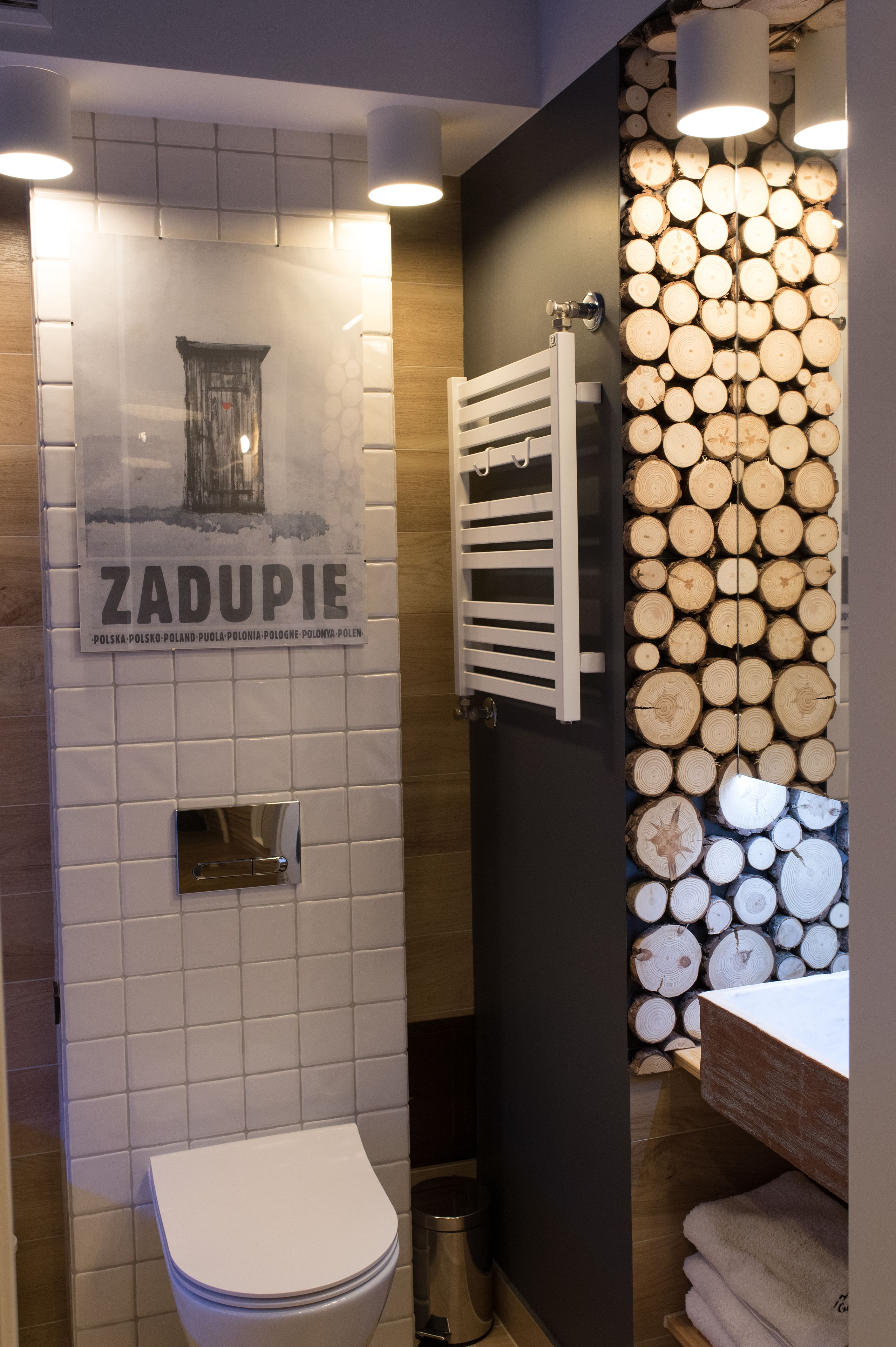A bathroom with a toilet, a towel rack, and a wall decorated with stacked logs.
