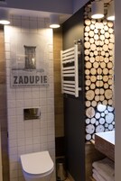 Un baño con inodoro, toallero y pared decorada con leña apilada.